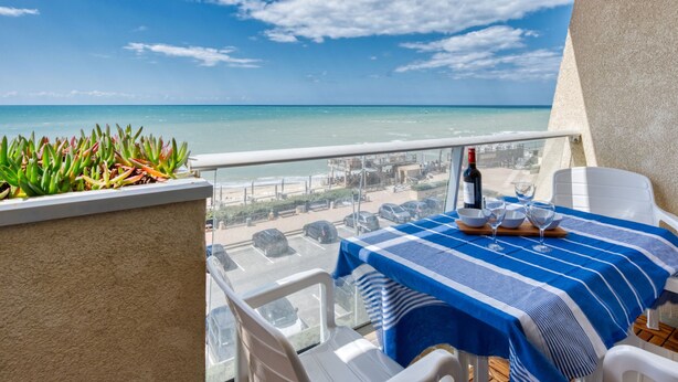 Un balcón con una mesa dispuesta para dos, con vistas a la playa y el mar.