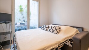 Een slaapkamer met een bed, een televisie en een schuifdeur naar een buitenruimte met stoelen en een tafel.