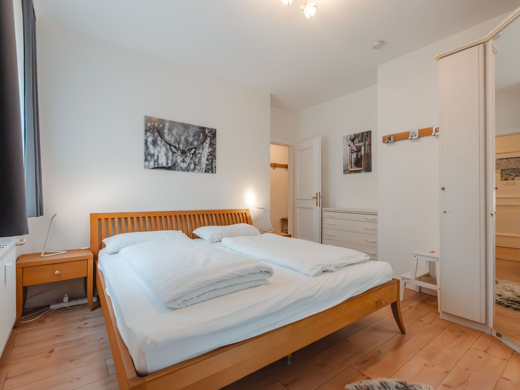 A bedroom with a wooden bed, white bedding, a nightstand, a desk, and a wardrobe.