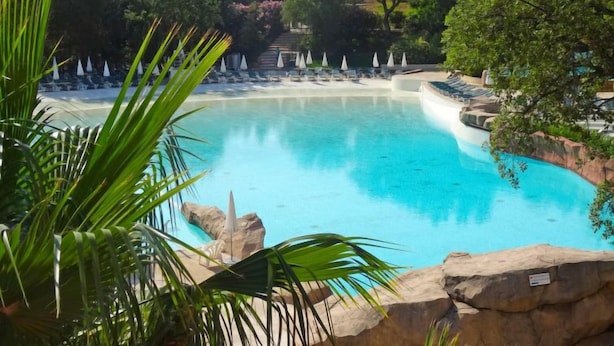 A clear blue pool surrounded by lounge chairs and umbrellas, with a rocky edge and lush greenery in the background. - Les Restanques Golfe Saint Tropez by Interhome (Grimaud)