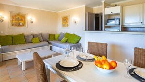 A modern living room with a sofa, dining table set for two, and a kitchen area with cabinets and a microwave. - Les Restanques Golfe Saint Tropez by Interhome (Grimaud)
