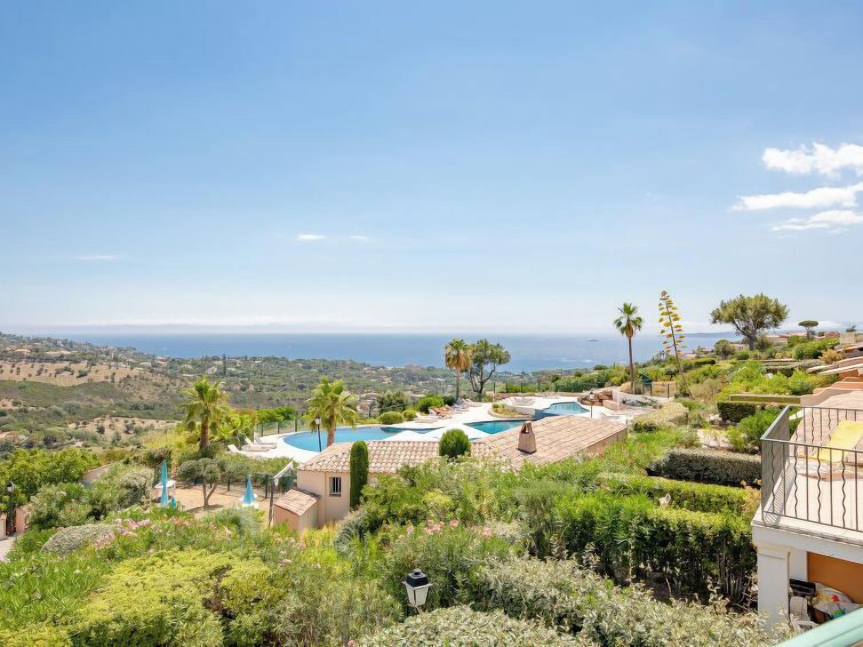 Ein Poolbereich mit Blick auf den Ozean, umgeben von Grünflächen und einer hügeligen Landschaft.