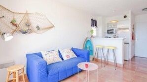 Een moderne woonkamer met een blauwe bank, een klein rond tafeltje en een keuken op de achtergrond.