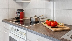 Una cocina moderna con gabinetes blancos, horno empotrado, estufa y tabla de cortar con tomates y un cuchillo.