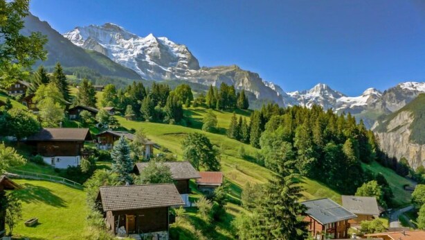 Un paisaje montañoso con casas ubicadas entre árboles, con vistas a picos nevados.