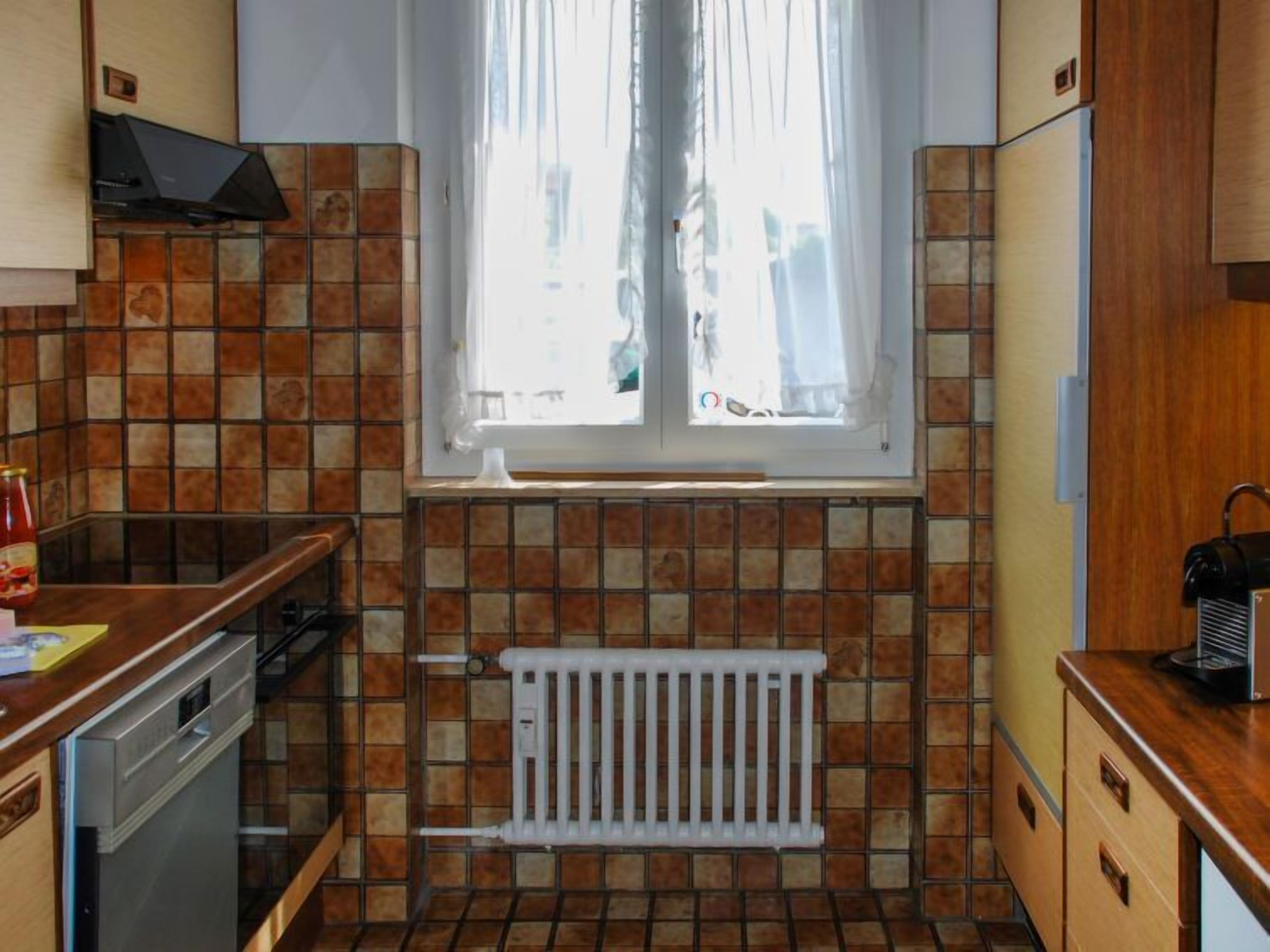 Cozinha compacta com janela, painel de azulejos e armários de madeira.