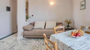 Ein gemütlicher Wohnbereich mit einer Couch, einem Esstisch mit zeitungsbedeckter Tischdecke und einer Obstschale.