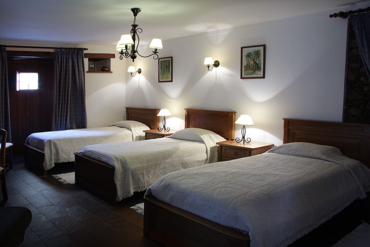 A hotel room with three single beds, a chandelier, wall-mounted lamps, and a painting.