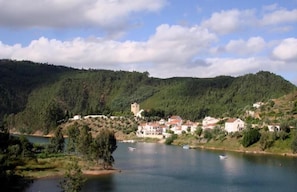 A lakeside village with buildings and a tower on a hillside. - Casa da Eira - Turismo Rural (Lousa)