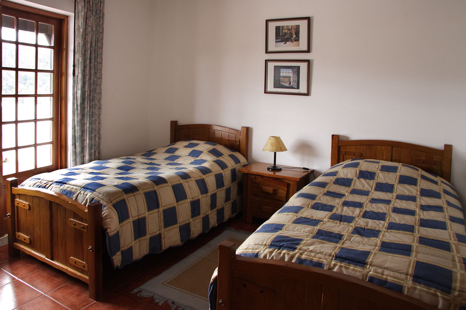 A bedroom with two wooden beds, a nightstand with a lamp, and a window with curtains.