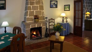 A cozy living room with a stone fireplace, a dining table with cards, and a vase with flowers. - Casa da Eira - Turismo Rural (Lousa)