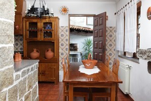 A rustic kitchen with a wooden table, terracotta pots, and a hanging light fixture. - Casa da Eira - Turismo Rural (Lousa)