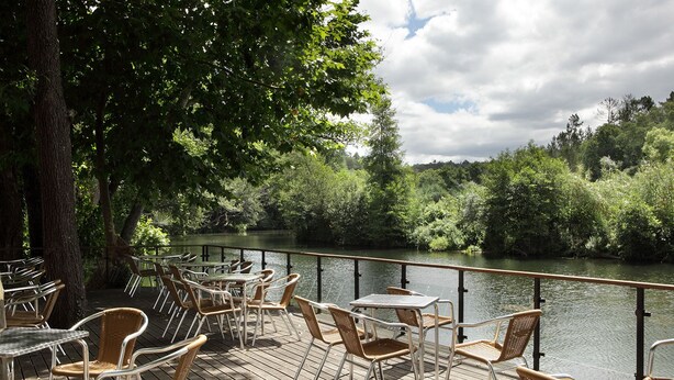 An outdoor dining area with tables and chairs overlooking a river, surrounded by trees. - Casa da Eira - Turismo Rural (Lousa)