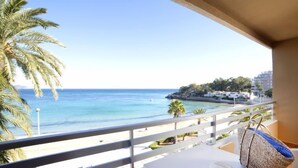 Un balcón con vista al mar, un sombrero y un bolso tejido sobre una mesa.