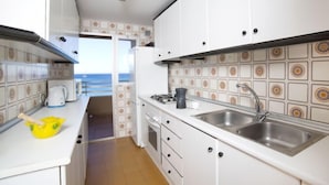 Cocina compacta con armarios blancos, pileta de acero inoxidable y vista al mar a través de una puerta abierta.