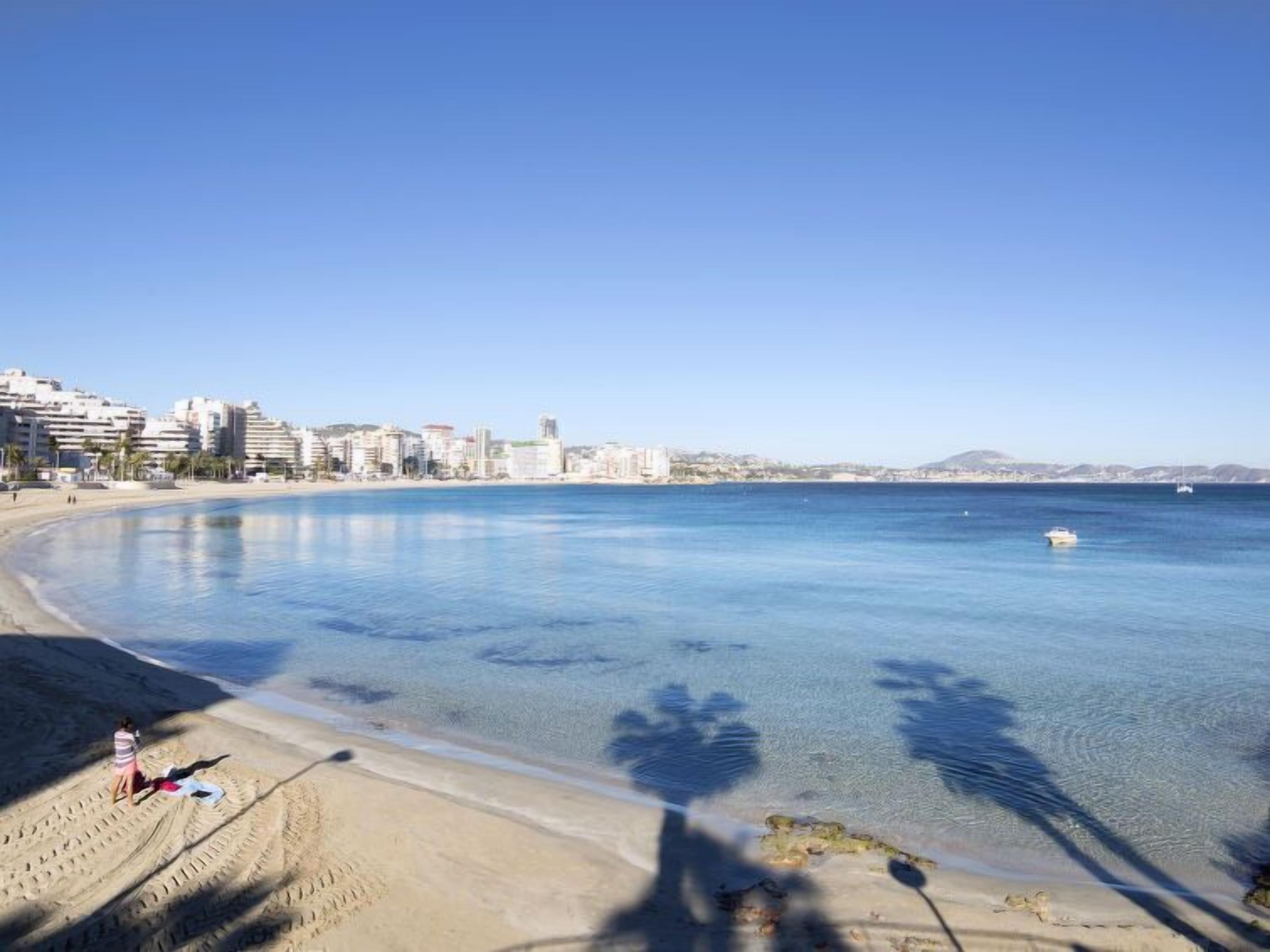 A coastal cityscape with a clear blue sky, a sandy beach, and a calm sea.