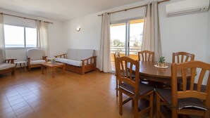 Amplia sala de estar con sofá, sillas, mesa de comedor y vistas a través de grandes ventanales.