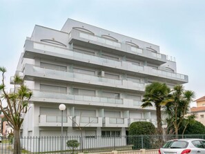 Un immeuble à plusieurs étages doté de balcons, d’un toit plat et d’une entrée fermée par un portail.