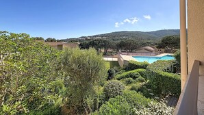 Une vue sur une piscine entourée d’une végétation bien entretenue et de bâtiments aux toits recouverts de tuiles rouges.