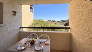 Un balcon avec une table dressée pour deux personnes, une petite lampe fixée au mur et une vue sur les bâtiments et les arbres.