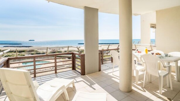 A balcony with a view of the beach and ocean, white plastic chairs, and a table with a drink. - Le Sunset/Cap Sud by Interhome (Cap d'Agde)