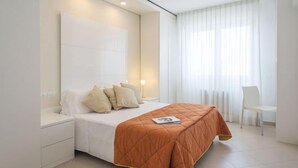 A modern bedroom with a bed, bedside tables, a chair, and a large window with curtains.