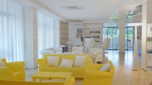A bright, modern lounge area with yellow sofas and white tables, large windows, and a visible staircase leading to another level.