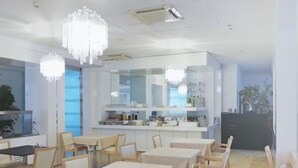 A modern dining area with wooden tables and chairs, a kitchen in the background, and a large mirror above the counter.