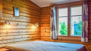 Una camera in legno con un letto, un comodino, una lampada a muro e una finestra con tende.