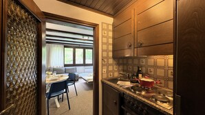Une cuisine compacte équipée d’une cuisinière, d’un évier et de placards. On aperçoit un coin repas avec une table et des chaises à travers une porte ouverte.