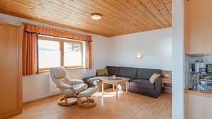 A cozy living room with a sofa, a chair, and a small table. There is a window with curtains and a view of the outside. - Voithofer by Interhome (Königsleiten)