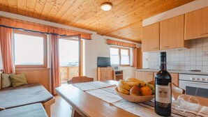 A cozy room with a wooden ceiling, a dining table with a bottle of wine, a bowl of fruit, and a TV in the background. - Voithofer by Interhome (Königsleiten)