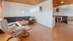 A modern living room with a wooden ceiling, a dark grey sofa, a white armchair, and a small table. - Voithofer by Interhome (Königsleiten)
