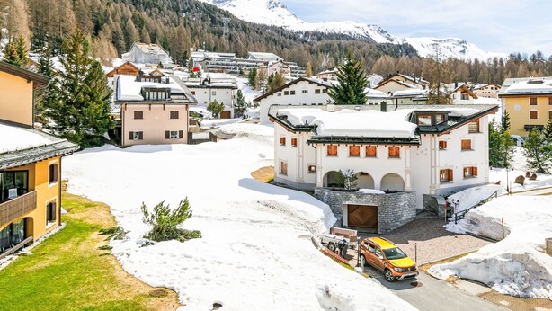 A snow-covered village with traditional architecture, a central building with a stone facade, and a mountain backdrop. - Residenza Chesa Margun 15-5 by Interhome (Silvaplana-Surlej)