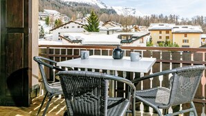 A balcony with wicker chairs and a table, overlooking a snowy mountain and residential buildings. - Residenza Chesa Margun 15-5 by Interhome (Silvaplana-Surlej)