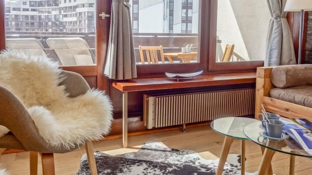 A cozy room with a view of mountains, a wooden desk, a fur chair, a glass table, and a sofa. - Le Prariond (Val Claret) by Interhome (Tignes)