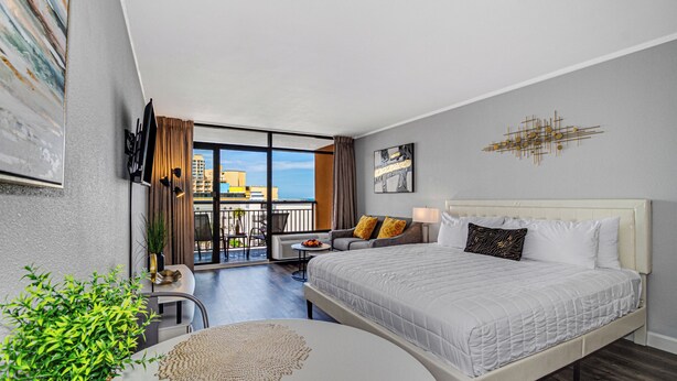 A modern hotel room with a large bed, a balcony with a view, a seating area, and a dining table. - Ideal Oceanview Studio Getaway! Amenities Galore (Myrtle Beach)