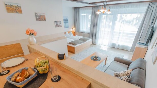 A modern hotel room with a wooden dining table, a sofa, a bed, and a large window with curtains. - Apartment Sepp by Interhome (Bad Hofgastein)