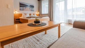 A modern hotel room with a wooden bed, a bedside table with a lamp, a large window with curtains, and a painting on the wall. - Apartment Sepp by Interhome (Bad Hofgastein)