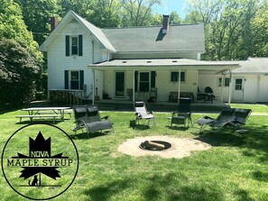 A two-story house with a covered porch, outdoor seating, and a fire pit. - Stay on a live operating maple syrup farm! (Hartstown)