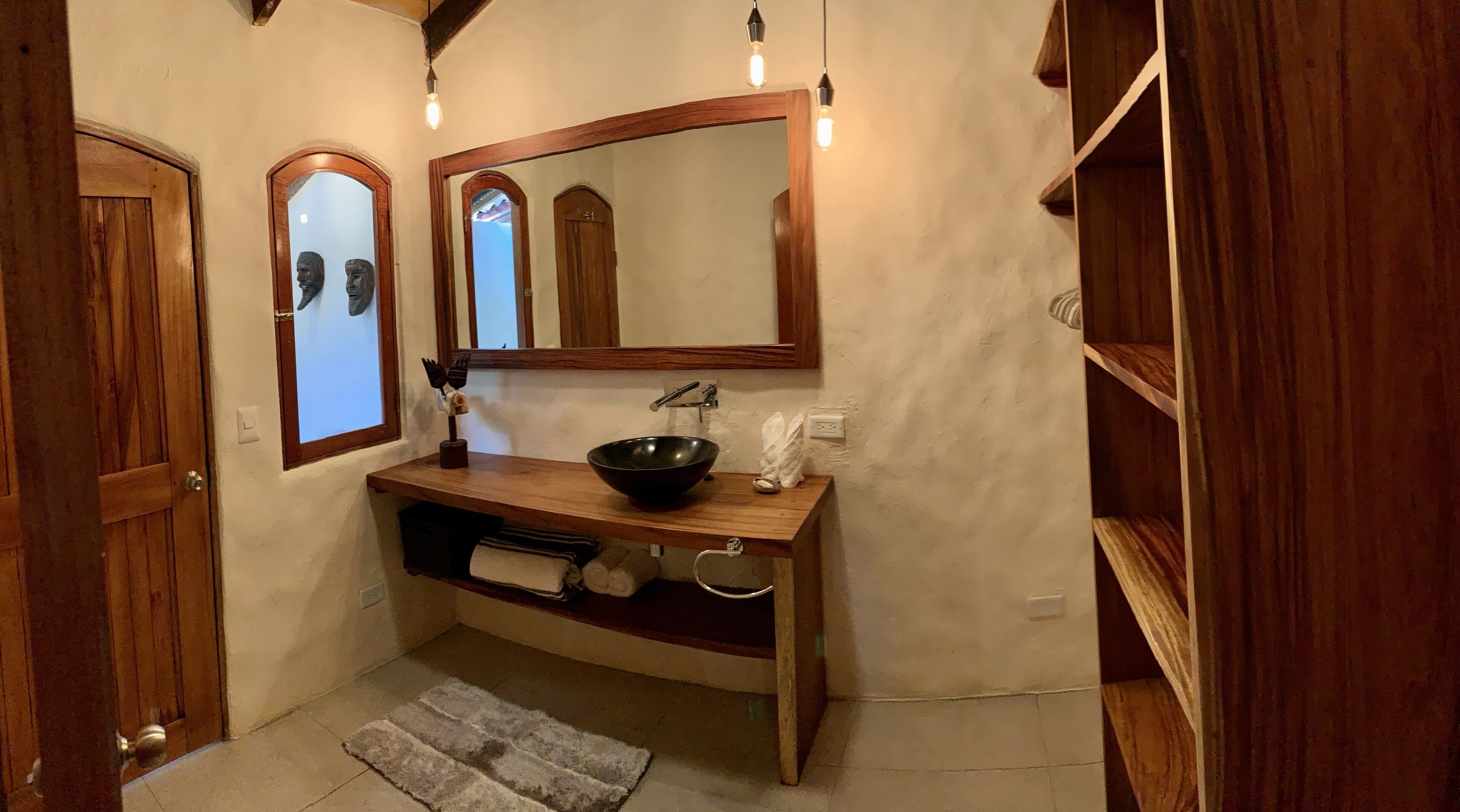 A bathroom with a wooden vanity, a black vessel sink, a mirror, and a towel rack.