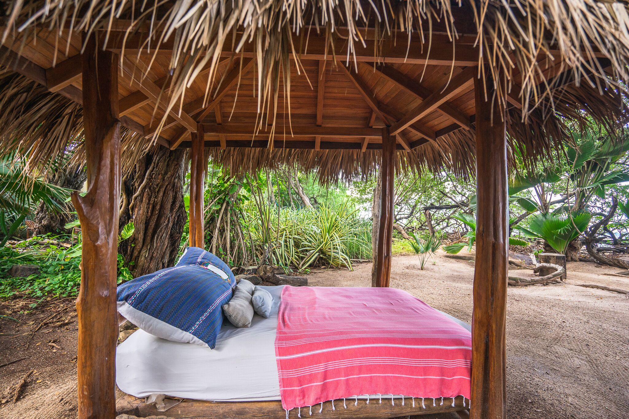 Una cabaña con techo de paja, una cama, almohadas y una manta.