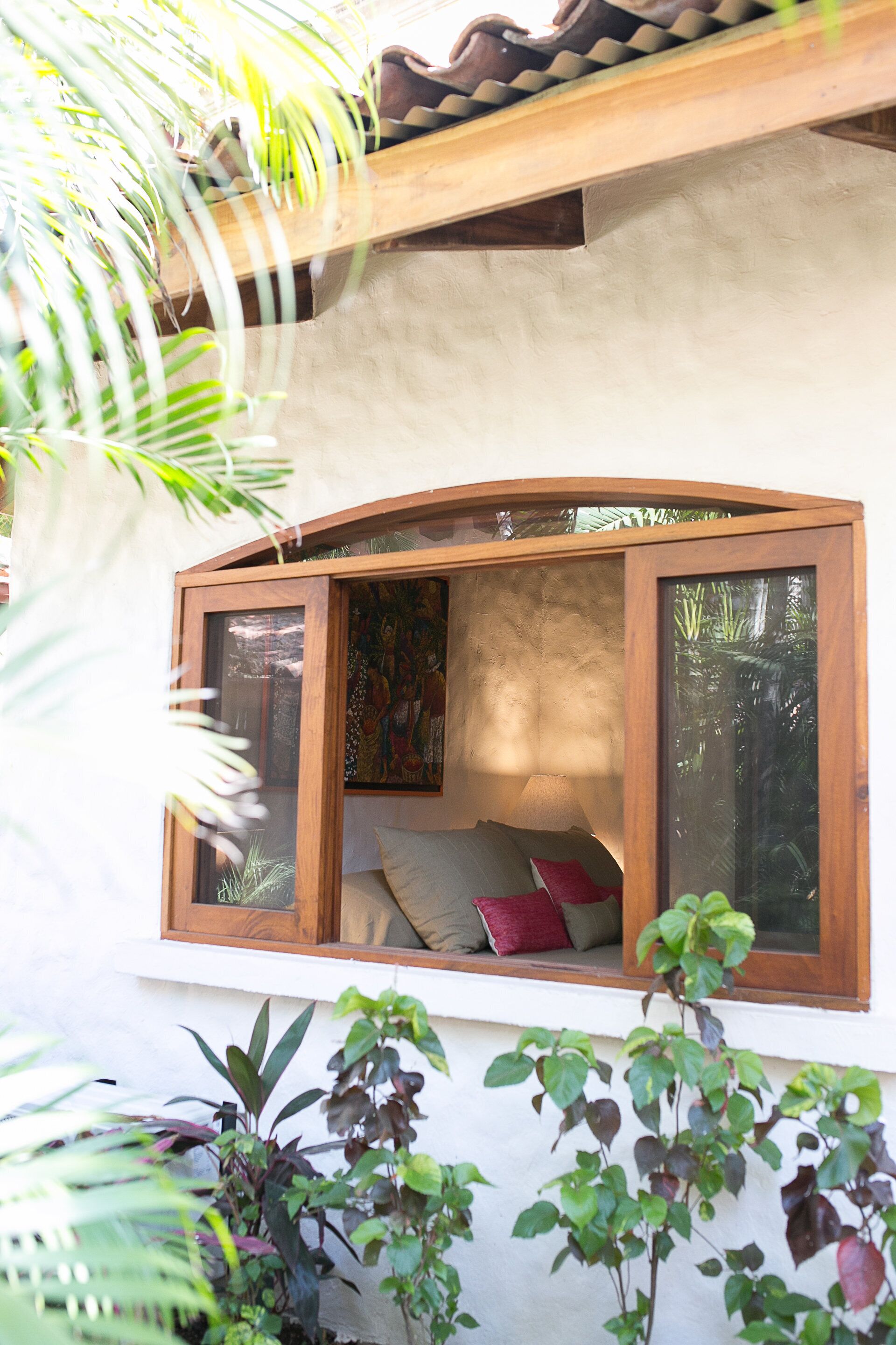 A room with a curved window, a bed with pillows, and a view of greenery outside.