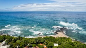 A coastal view with a beach, ocean waves, and dense greenery. - Sueno del Mar Beachfront Hotel (Tamarindo)