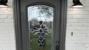Una puerta principal de color gris oscuro con un panel de vidrio decorativo y un buzón pequeño a la derecha.
