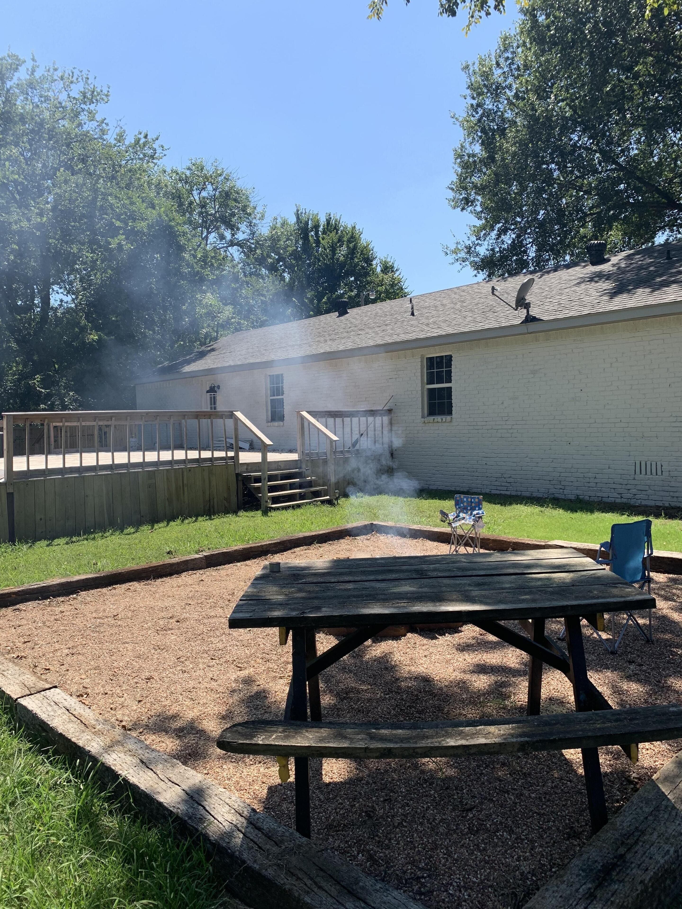 A backyard with a wooden deck, a picnic table, and a barbecue grill.