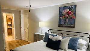 Un dormitorio ordenado con cama, almohadas, una mesita de noche, una lámpara y un cuadro en la pared.