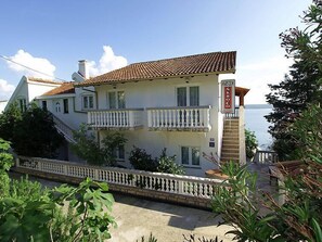 A two-story building with a balcony, a sign reading "SKROCO," and a view of the sea.