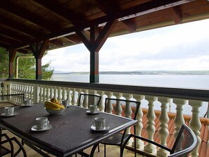 A covered outdoor seating area with a table set for two, overlooking a body of water.