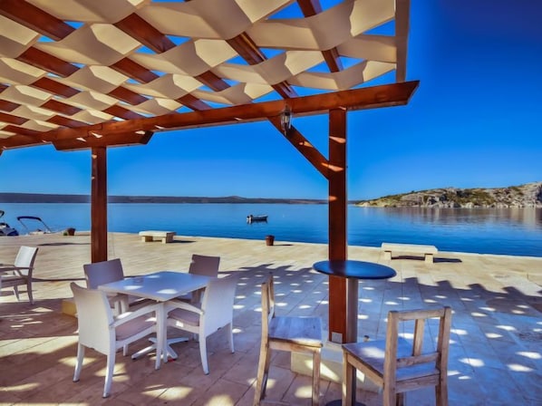 An outdoor terrace with a pergola, seating, and a view of the sea.